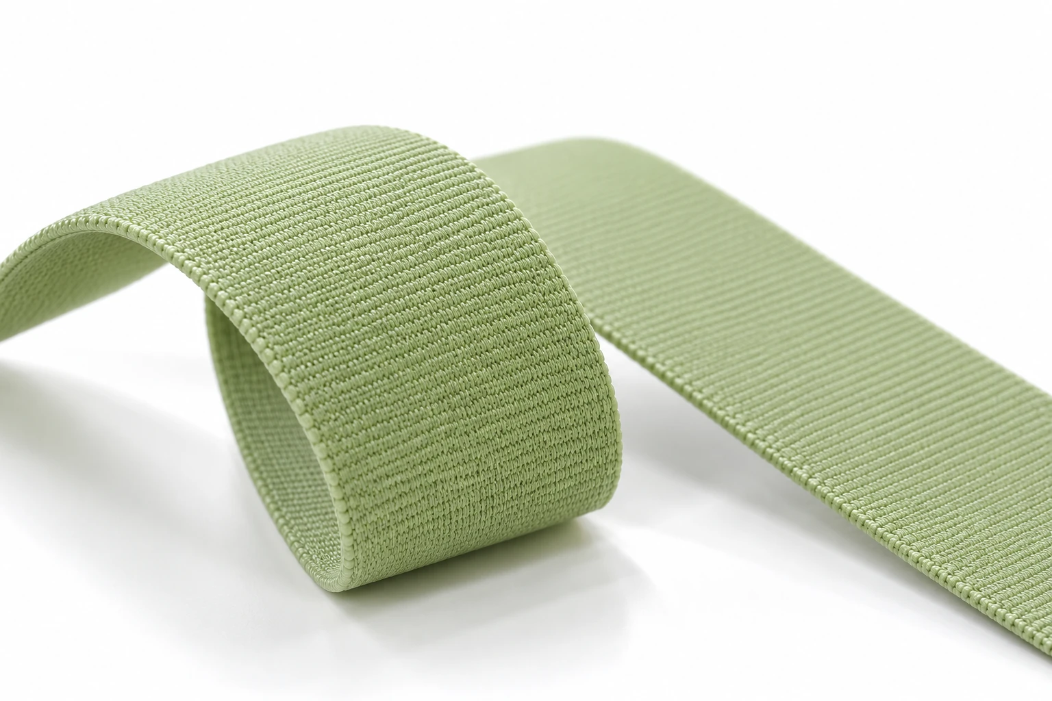 Pale sage-green elastic nylon webbing arranged in a soft loop on a white background, showing a fine woven surface.