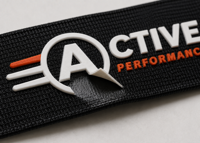 Silicone logo peeling from coated black webbing, showing adhesion failure at the interface.