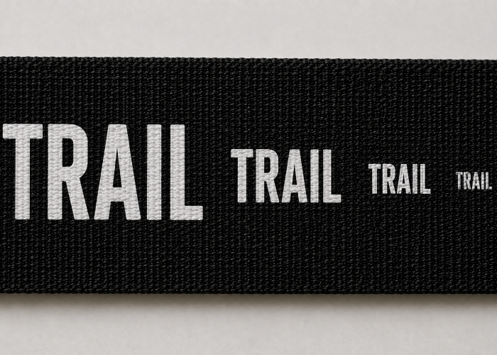 Same screen printed word shown at progressively smaller sizes on black woven webbing.